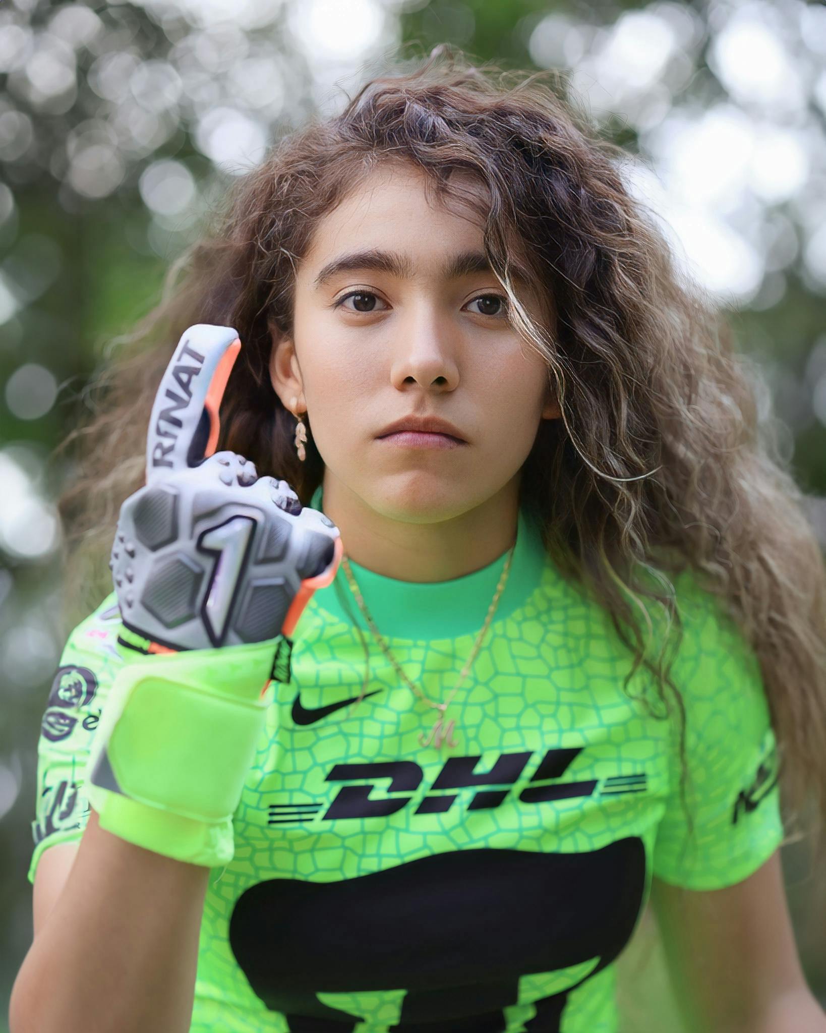 Portrait of a determined female soccer player in neon green sportswear with goalie glove raised.