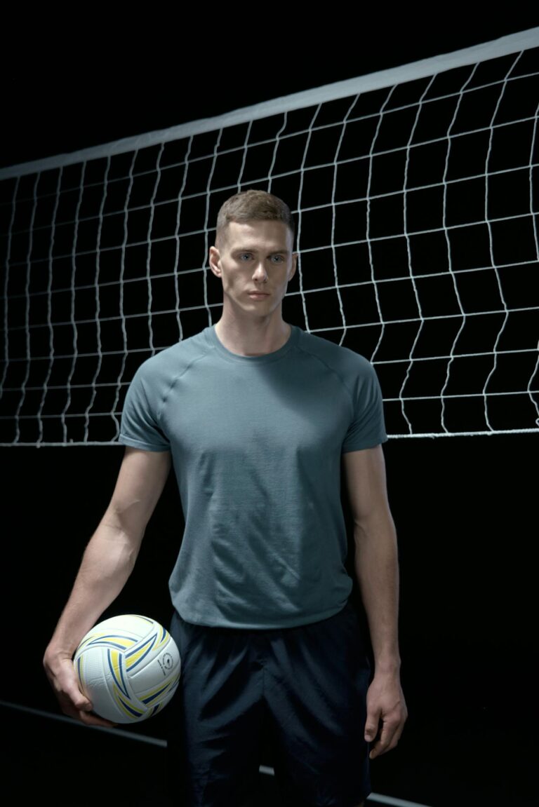 Portrait of a man holding a volleyball in front of a net, indoor sports setting.